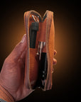Hand holding a brown leather tool pouch with a black tool inside on a dark background Japanese master oiled deer leather pouch with mimosa and quebracho tannins